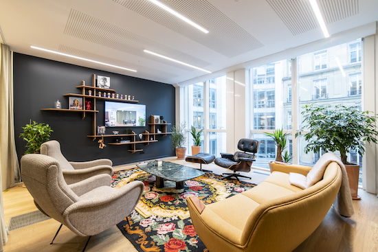 Aménagement d'un espace de convivialité dans un bureau professionnel pour se sentir comme à la maison. L'espace est composé de fauteuils, canapés et plantes pour offrir un côté chaleureux.